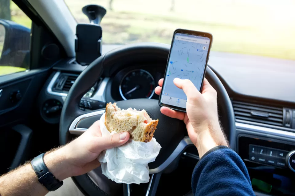 Close-up of person eating sandwich and texting while driving